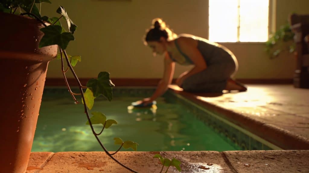 Femme agenouillée brosse le fond dune piscine verte